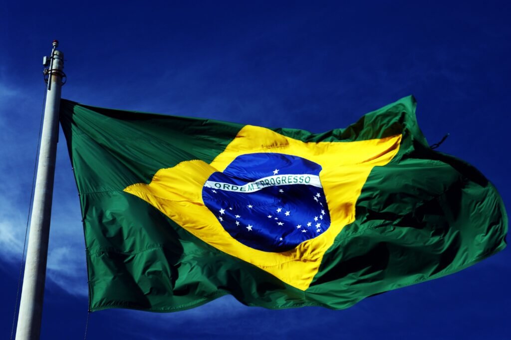 A dynamic shot of the Brazilian flag waving on a flagpole with a clear blue sky background.